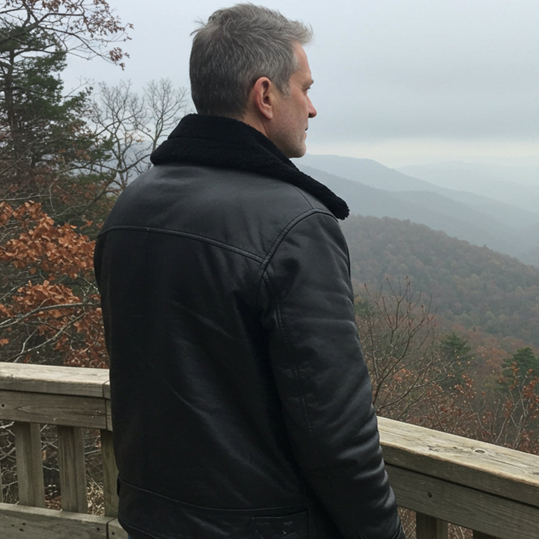 Man in a black leather jacket looking out over a misty forested area.