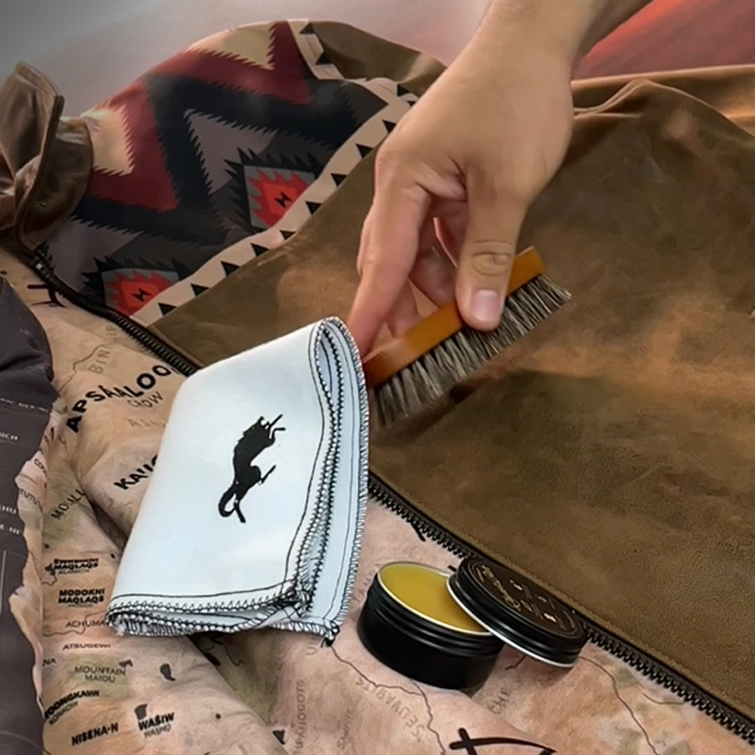 Person using a brush on leather with a cloth and container of leather care product.